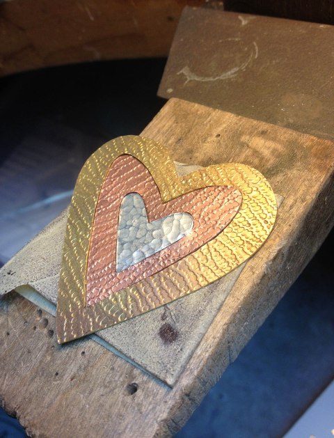This is a heart pendant in progress made by Lindy Hartig. Her piece is made of sterling silver, brass and copper. She textured each of the various metals for a more enhanced look.